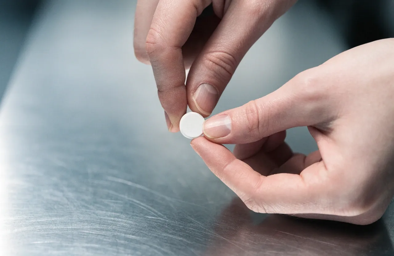 Close view of hands holding a plain unbranded caplet above a cleanroom bench
